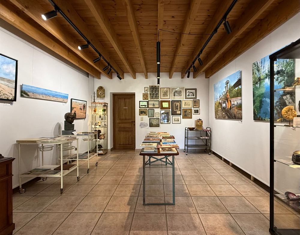 A white gallery room with paintings, a display case and a wall of framed prints